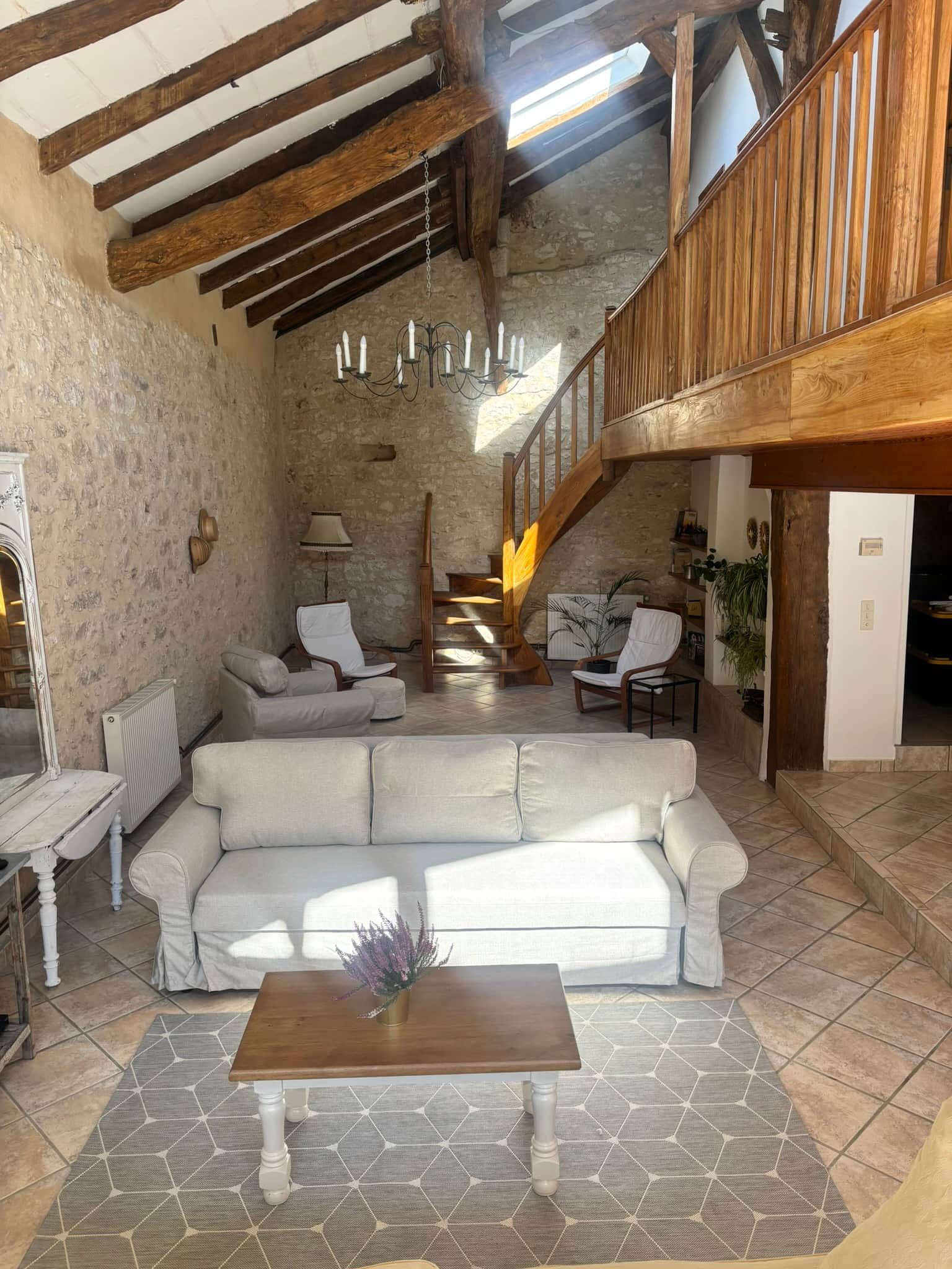 Un vaste espace de vie doté d’un plafond haut, de poutres apparentes, d’un canapé blanc central et d’une table basse en bois.