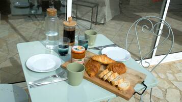 Een gedekte tafel met een bord, een kopje, een pot, een karaf, een croissant en een snijplank met sneetjes brood.