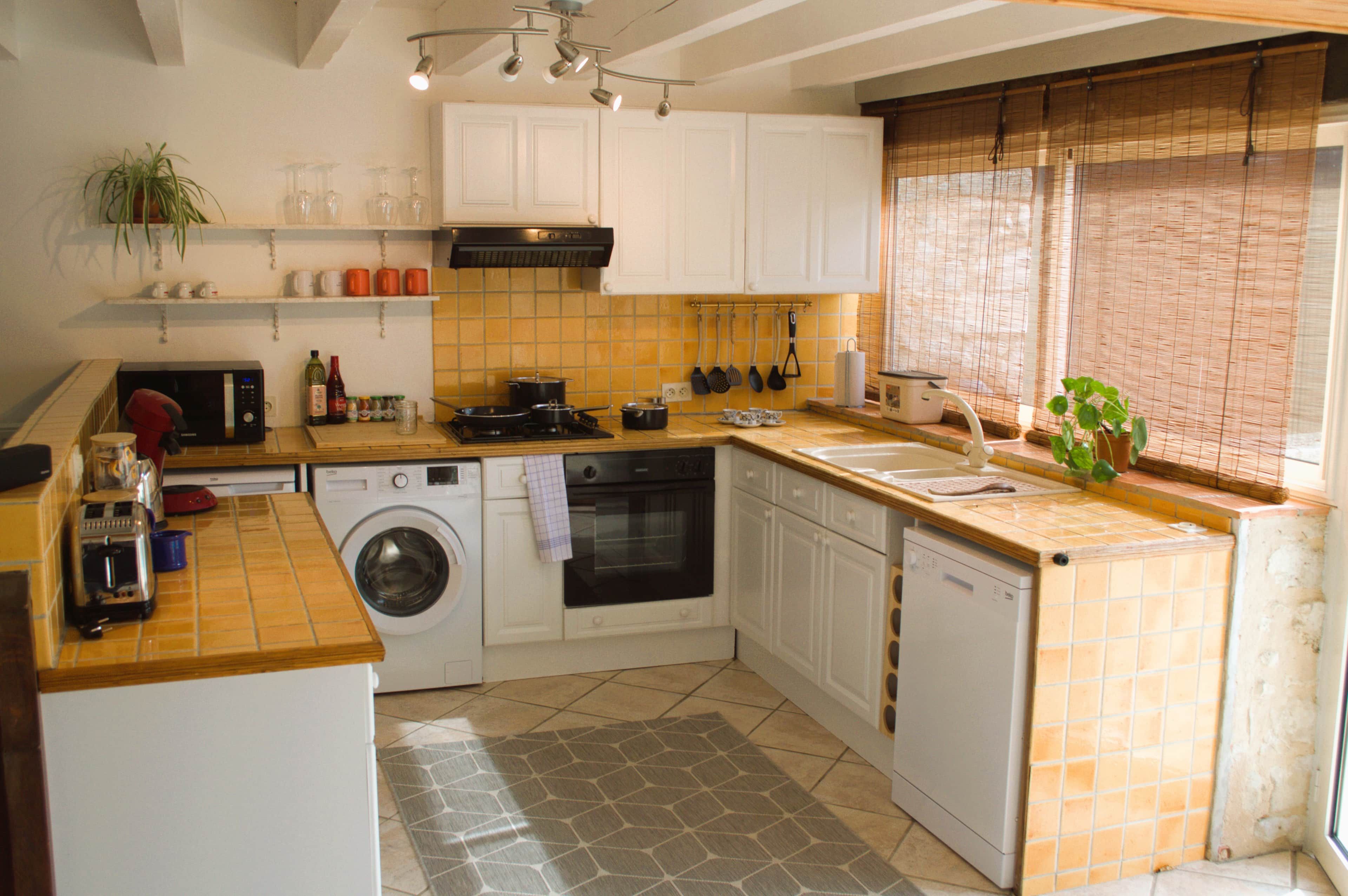 Een compacte keuken met een wasmachine, oven en diverse keukengerei op het aanrecht.