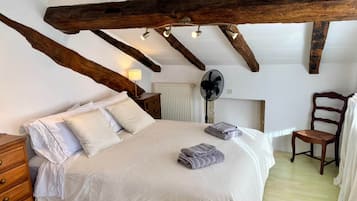 Ein Schlafzimmer mit einem großen Bett, Holzbalken, einer Heizung, einem Ventilator und einem Stuhl.