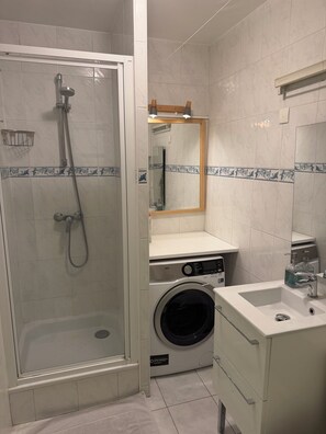 A compact bathroom with a glass-enclosed shower, a washing machine, and a sink with a mirror above it.