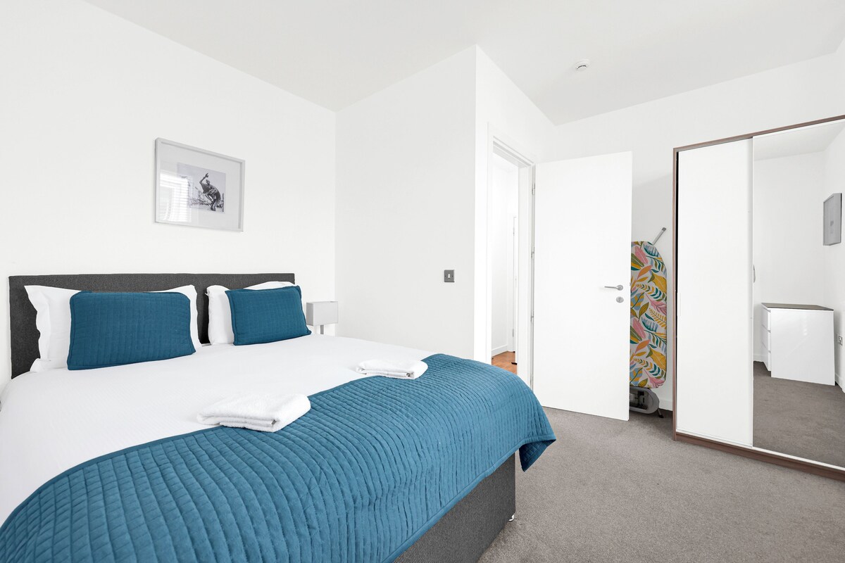 A modern bedroom with a large bed, a bedside table, a wardrobe, and a mirror.