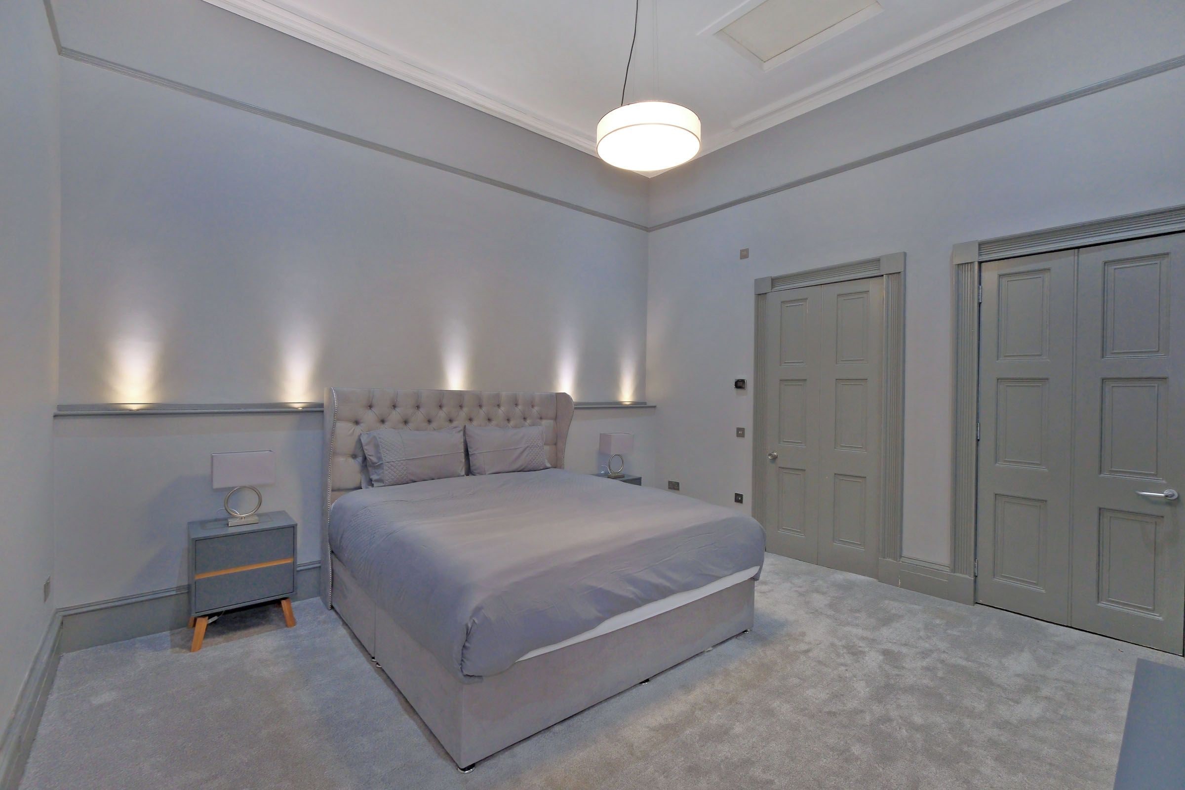 A bedroom with a large bed, bedside tables, a hanging light fixture, and double doors.