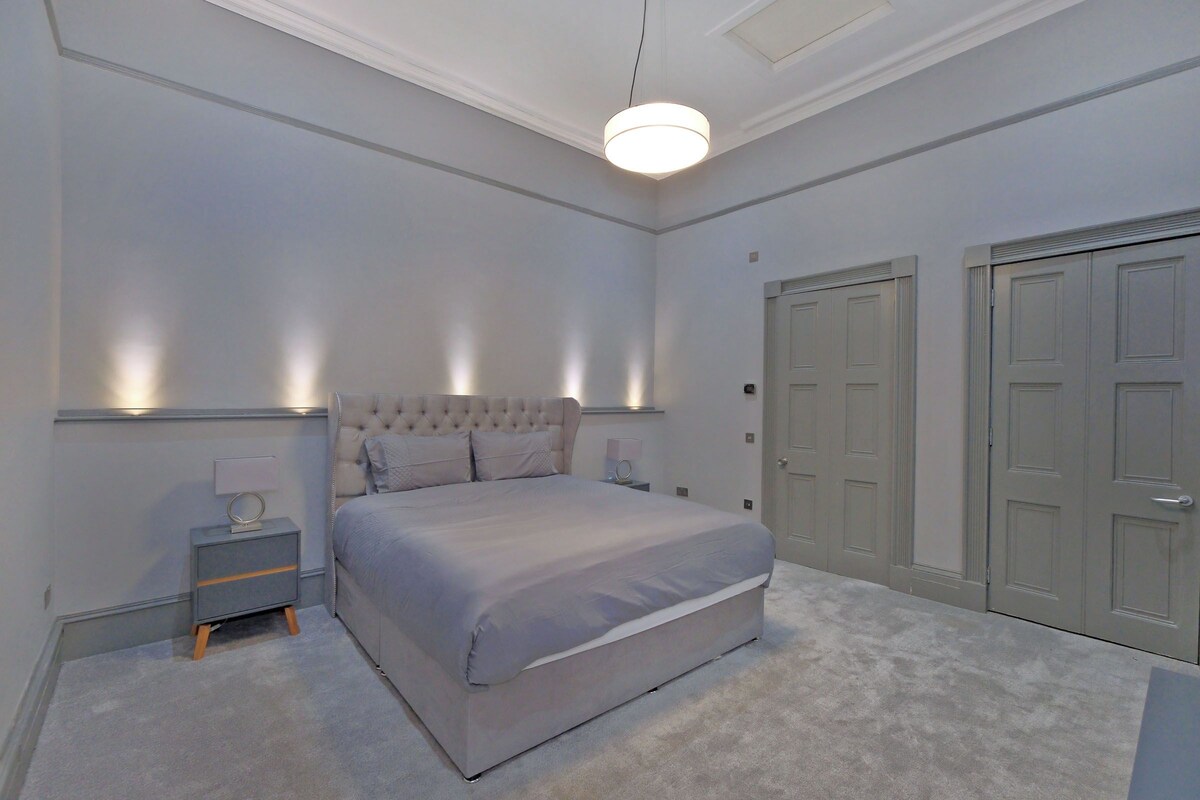 Ein Schlafzimmer mit einem großen Bett, Nachttischen, einer Hängeleuchte und Doppeltüren.