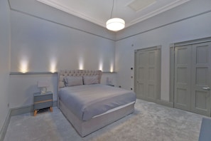 A bedroom with a large bed, bedside tables, a hanging light fixture, and double doors.