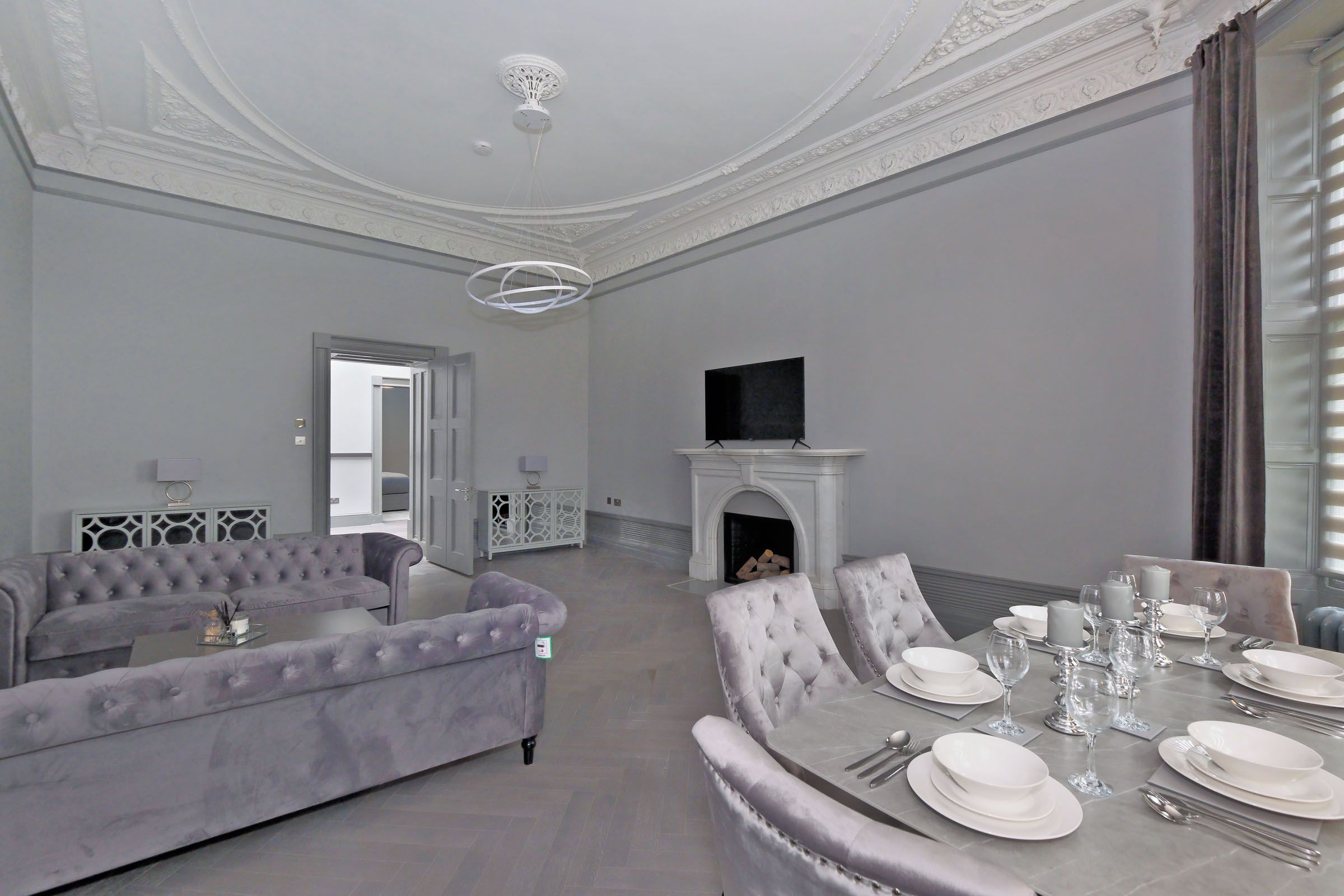 A spacious room with a fireplace, a television mounted above it, and a dining area set with white tableware.