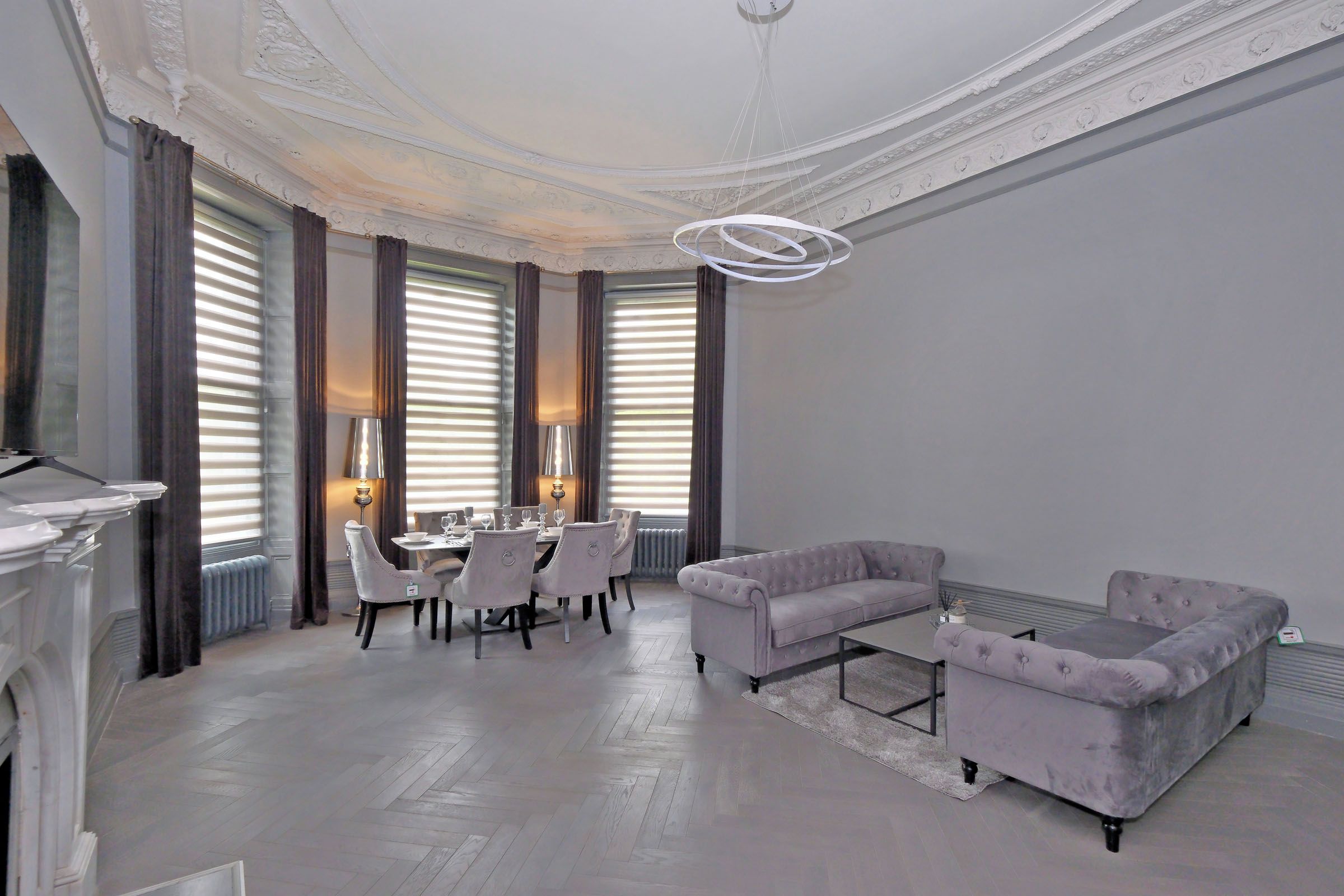 A spacious living room with a fireplace, a dining area with a table set for four, and a seating area with two sofas.