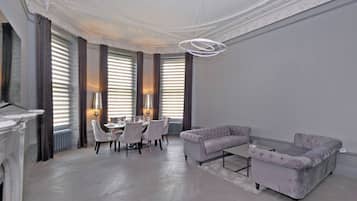 A spacious living room with a fireplace, a dining area with a table set for four, and a seating area with two sofas.