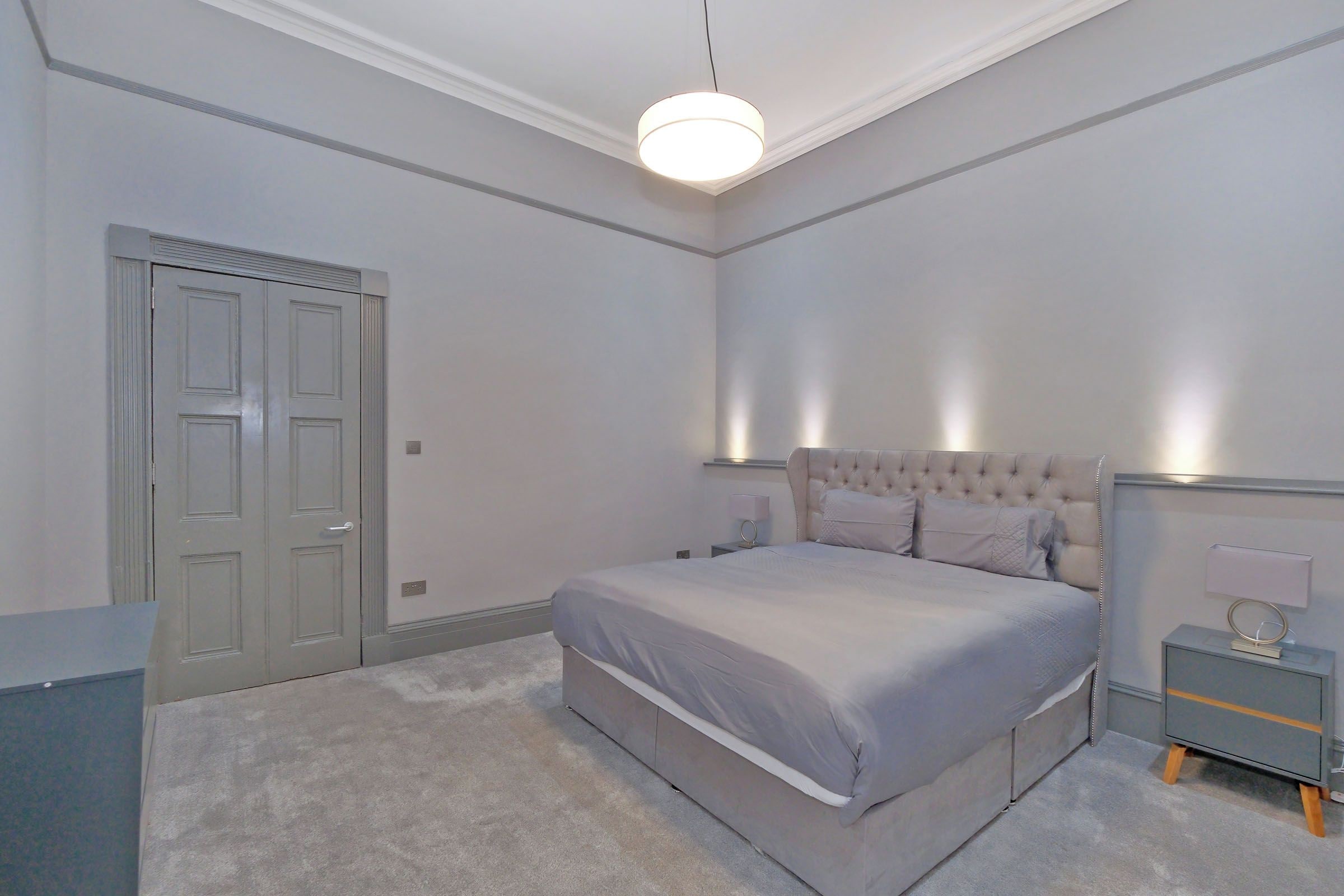 A bedroom with a bed, bedside tables, a nightstand, a door, and a light fixture.