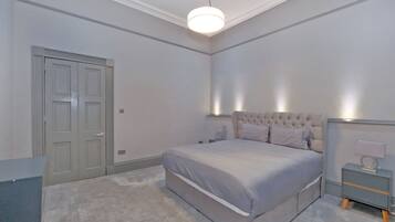 A bedroom with a bed, bedside tables, a nightstand, a door, and a light fixture.
