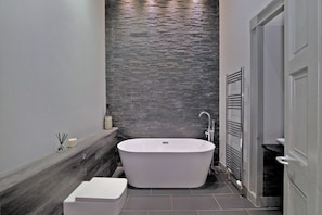 A modern bathroom with a freestanding bathtub, a toilet, and a shower area.