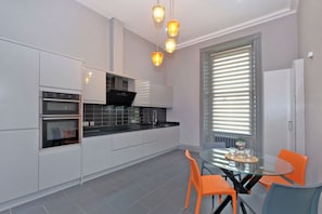Eine moderne Küche mit weißen Schränken, schwarzen Arbeitsplatten und einem Esstisch aus Glas mit orangefarbenen Stühlen.