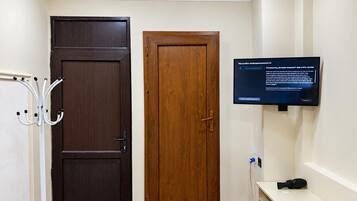 A room with a dark wooden door, a lighter wooden door, a mounted television, and a small table with a remote control.