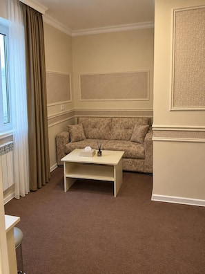 Ein Wohnzimmer mit einem beigefarbenen Sofa, einem weißen Couchtisch und einem Fenster mit Vorhängen.