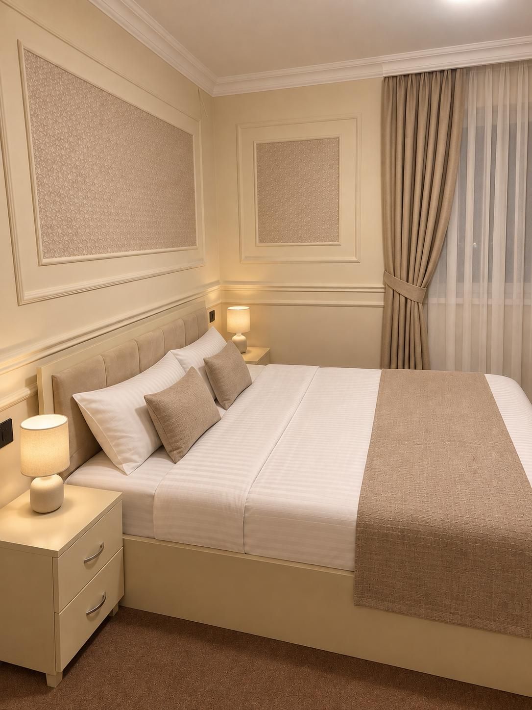A hotel room with a large bed, two bedside tables with lamps, a headboard, and a window with curtains.