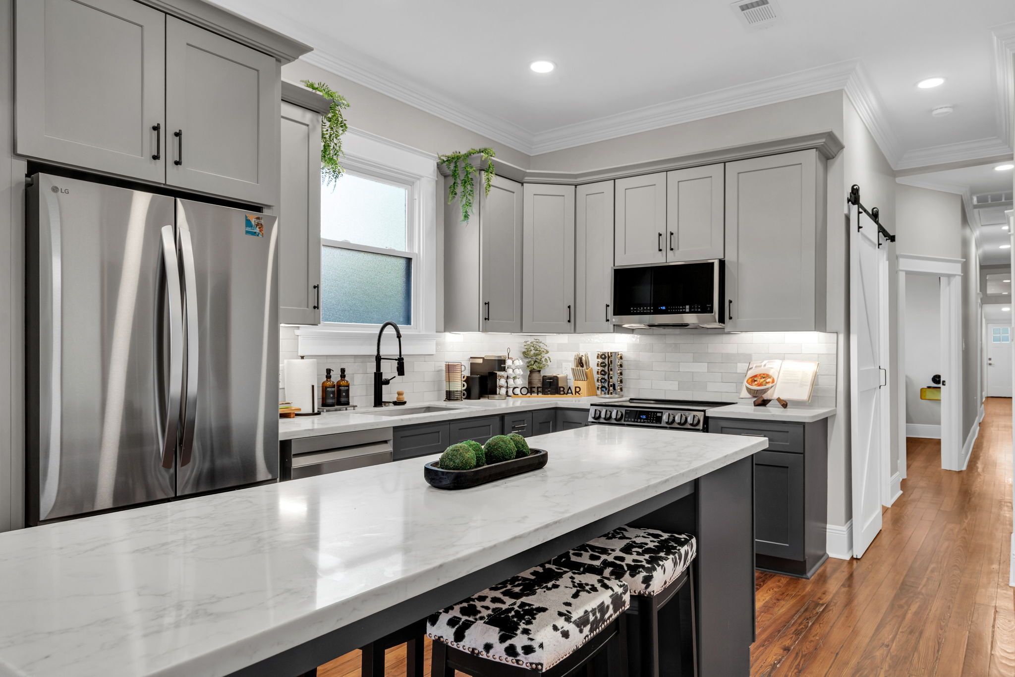 A modern kitchen with grey cabinetry, a stainless steel refrigerator, a built-in microwave, and a central island with a bench.