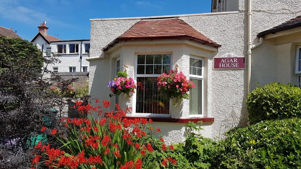Un edificio con un letrero que dice 'AGAR HOUSE' y una ventana decorada con macetas colgantes de flores.