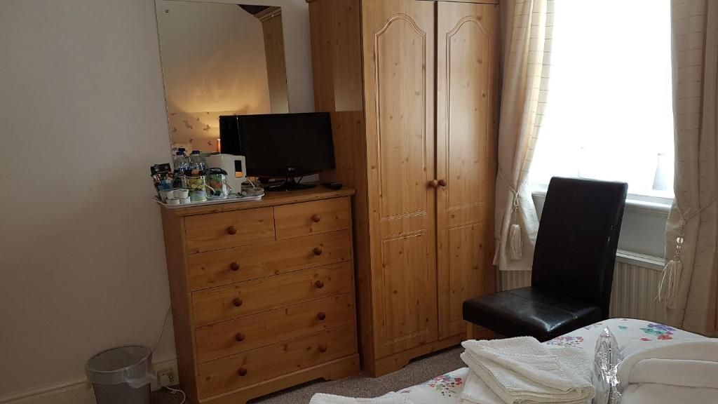 A bedroom with a wooden wardrobe, a television on a dresser, a black chair, and a bed with a floral bedspread.
