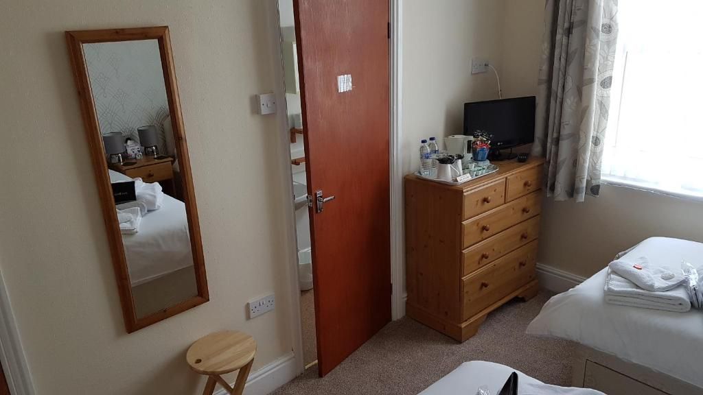 Quarto de hotel com cama, cômoda de madeira, televisão e espelho.
