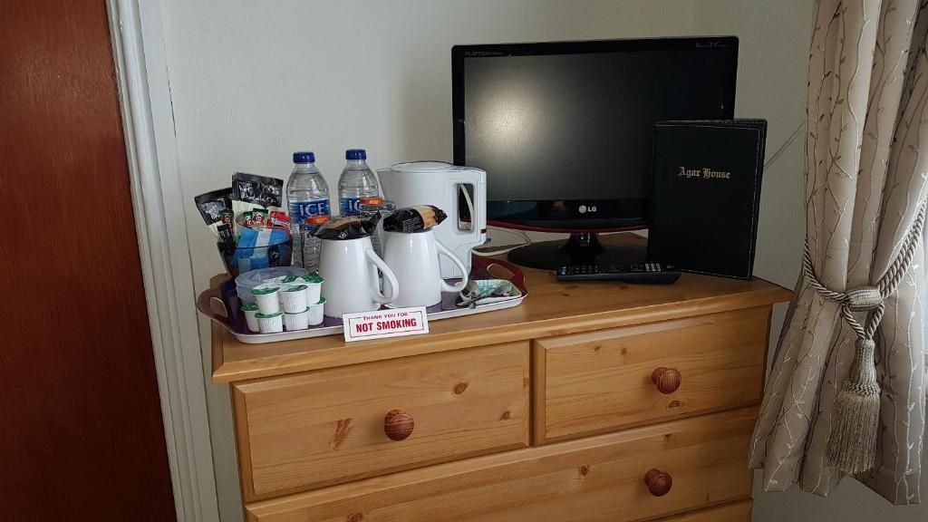 A wooden dresser with a 'Thank you for not smoking' sign, a television, a coffee maker, and a book titled 'Agur House'.