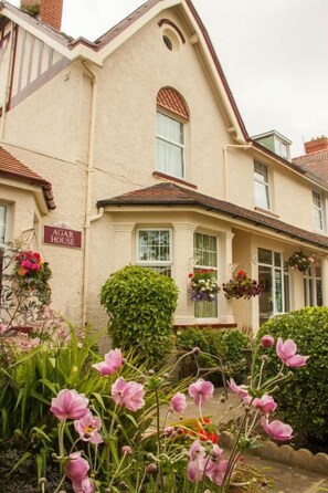 Un edificio con un letrero que dice 'AGAR HOUSE' y un jardín bien cuidado con flores rosas.