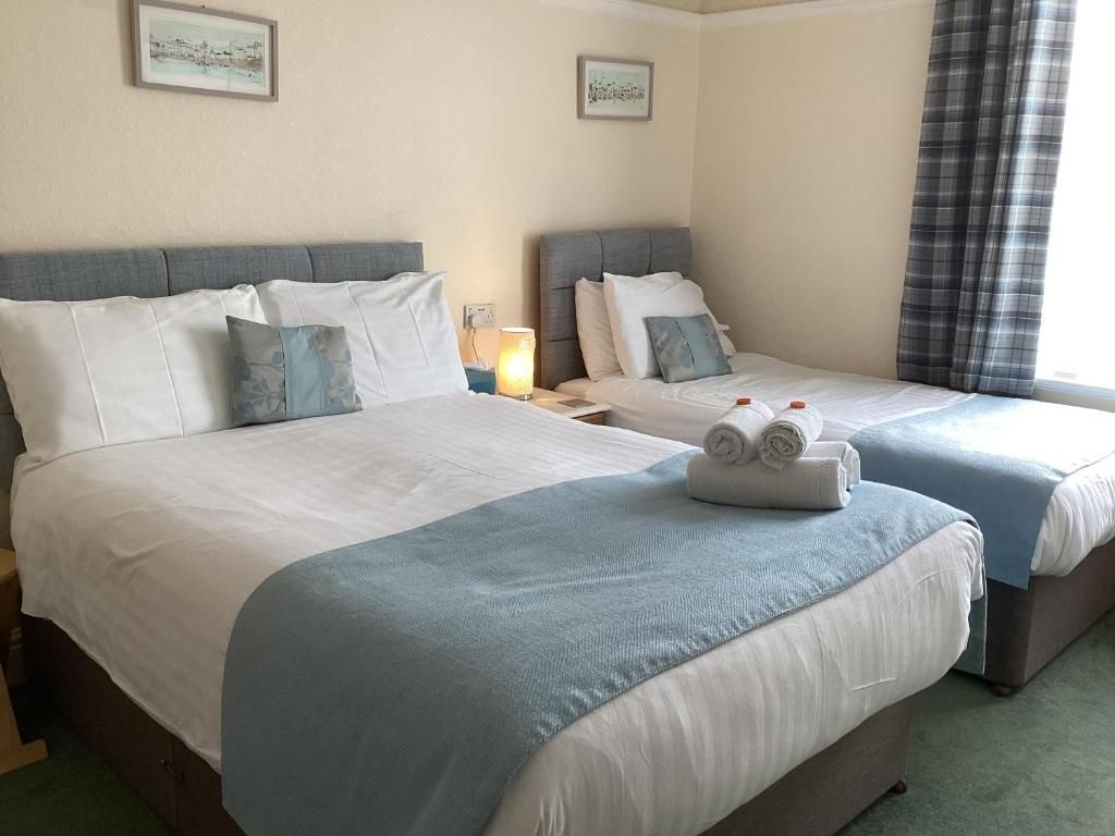 A hotel room with two beds, each with a headboard, a nightstand with a lamp, and a window with curtains.