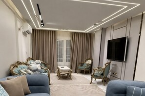 Ein modernes Wohnzimmer mit einem Flachbildfernseher, verzierten Stühlen und einem gemusterten Teppich.