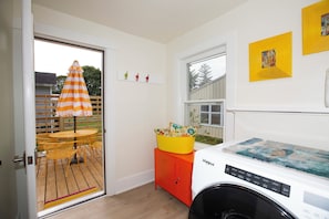 Un cuarto de lavandería con lavadora, una mesa de madera con sillas y una puerta que da a un espacio exterior con sombrilla.