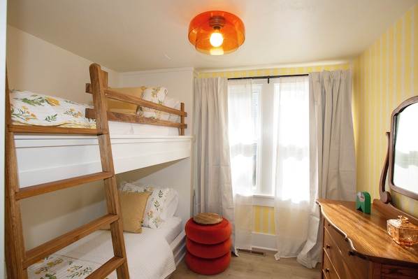 Una habitación con una cama individual superpuesta, una escalera de madera, un taburete pequeño rojo, un aparador de madera y un espejo.