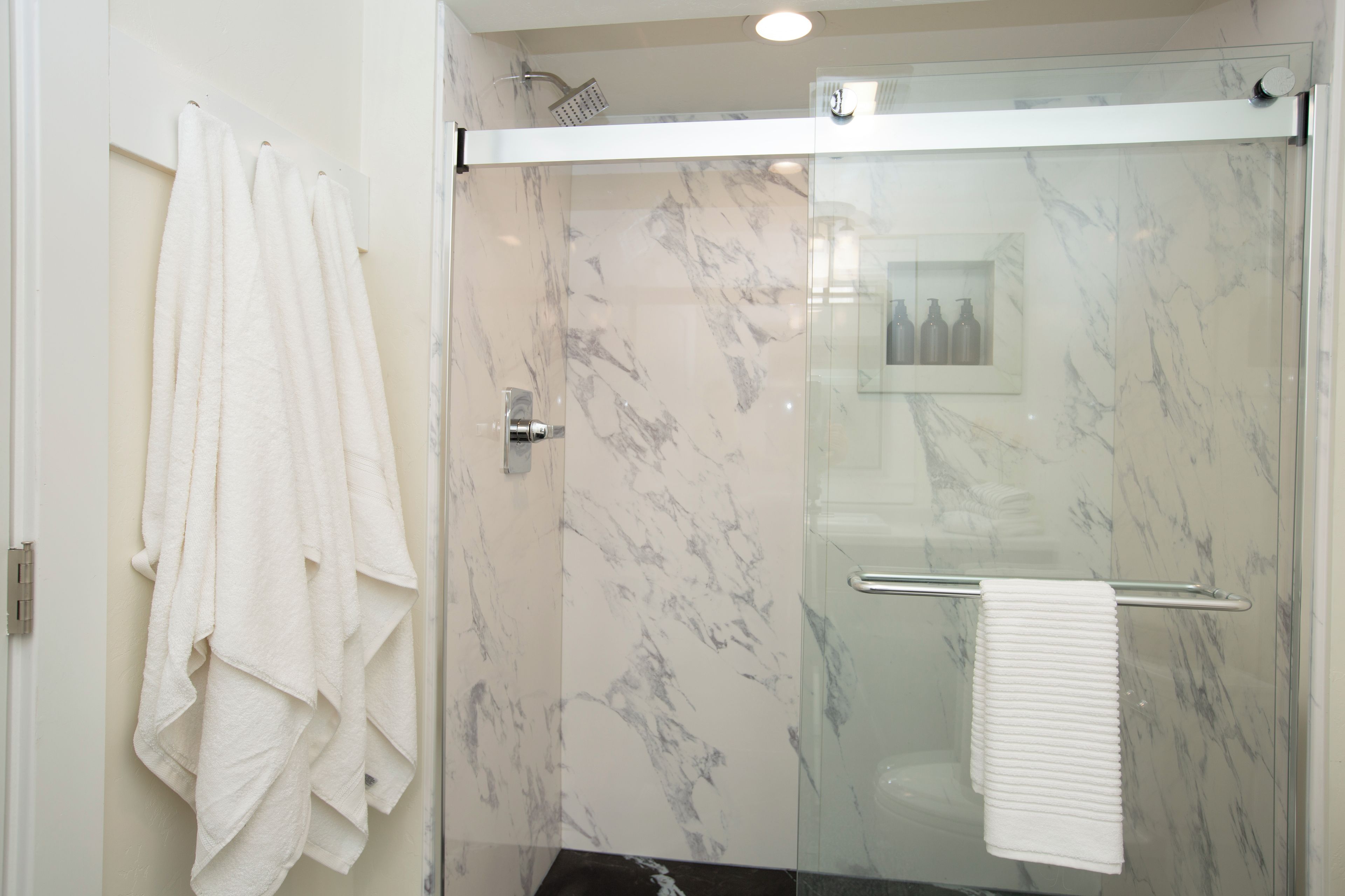 Une salle de bain moderne dotée d’une cabine de douche en verre, de murs en marbre et d’un porte-serviettes avec plusieurs serviettes.