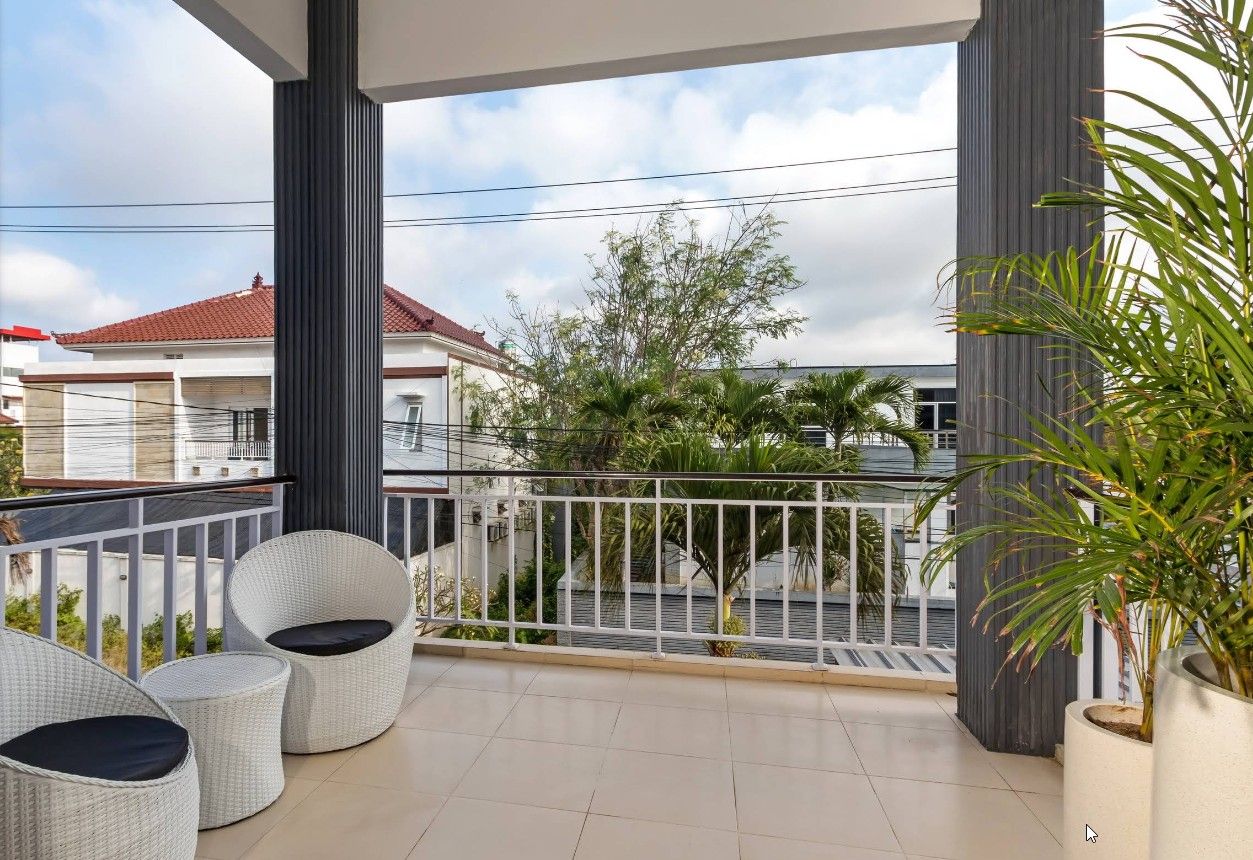 Un balcon avec deux fauteuils en osier, une balustrade et un pot de fleurs.