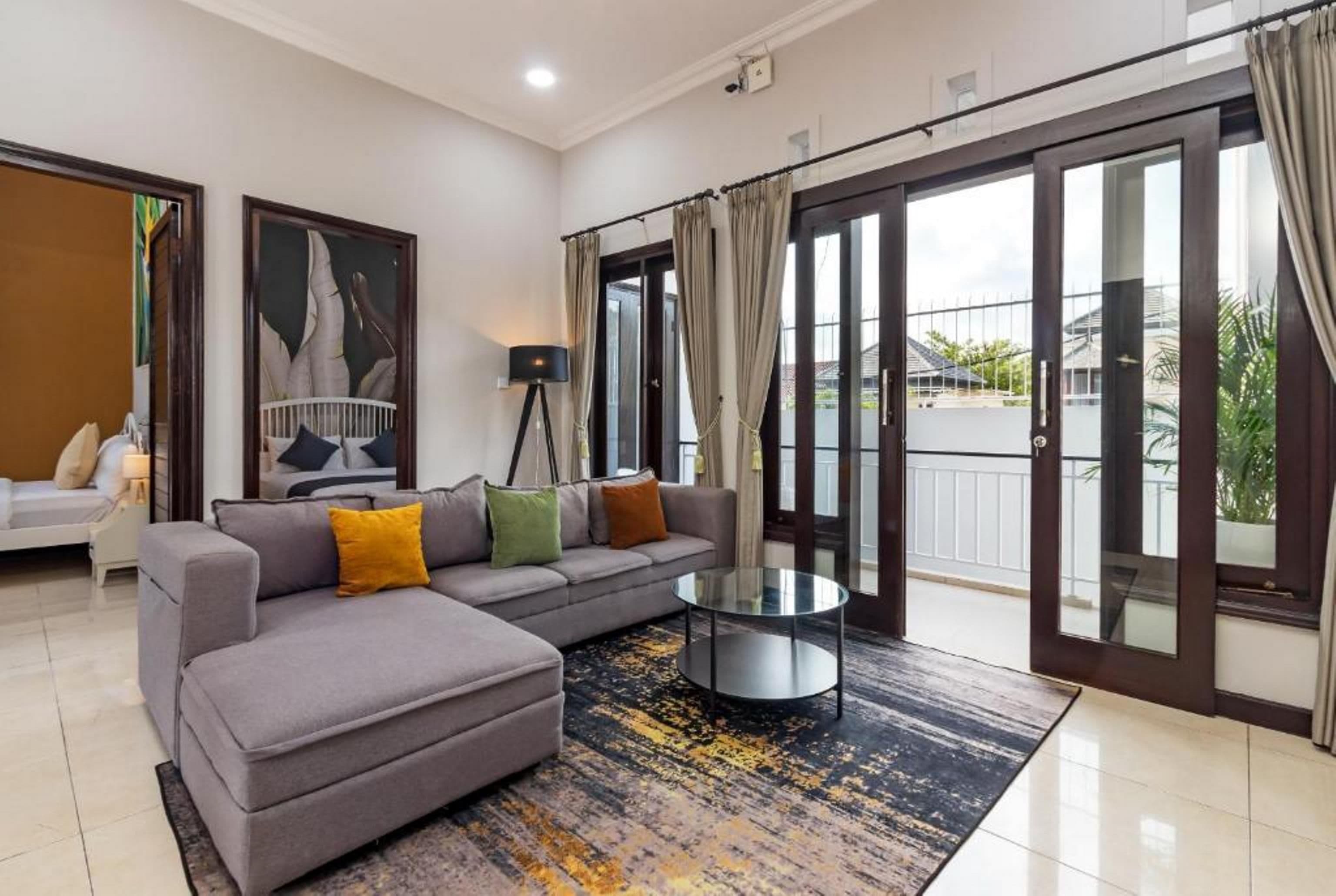 A modern living room with a grey sectional sofa, a glass coffee table, and a large painting on the wall.