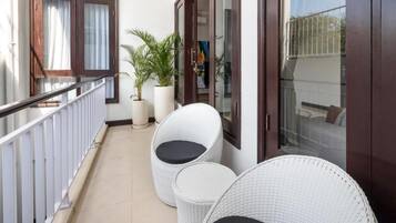 Un balcón con dos sillas de mimbre, una planta en maceta y un ventanal de vidrio que da a una terraza.