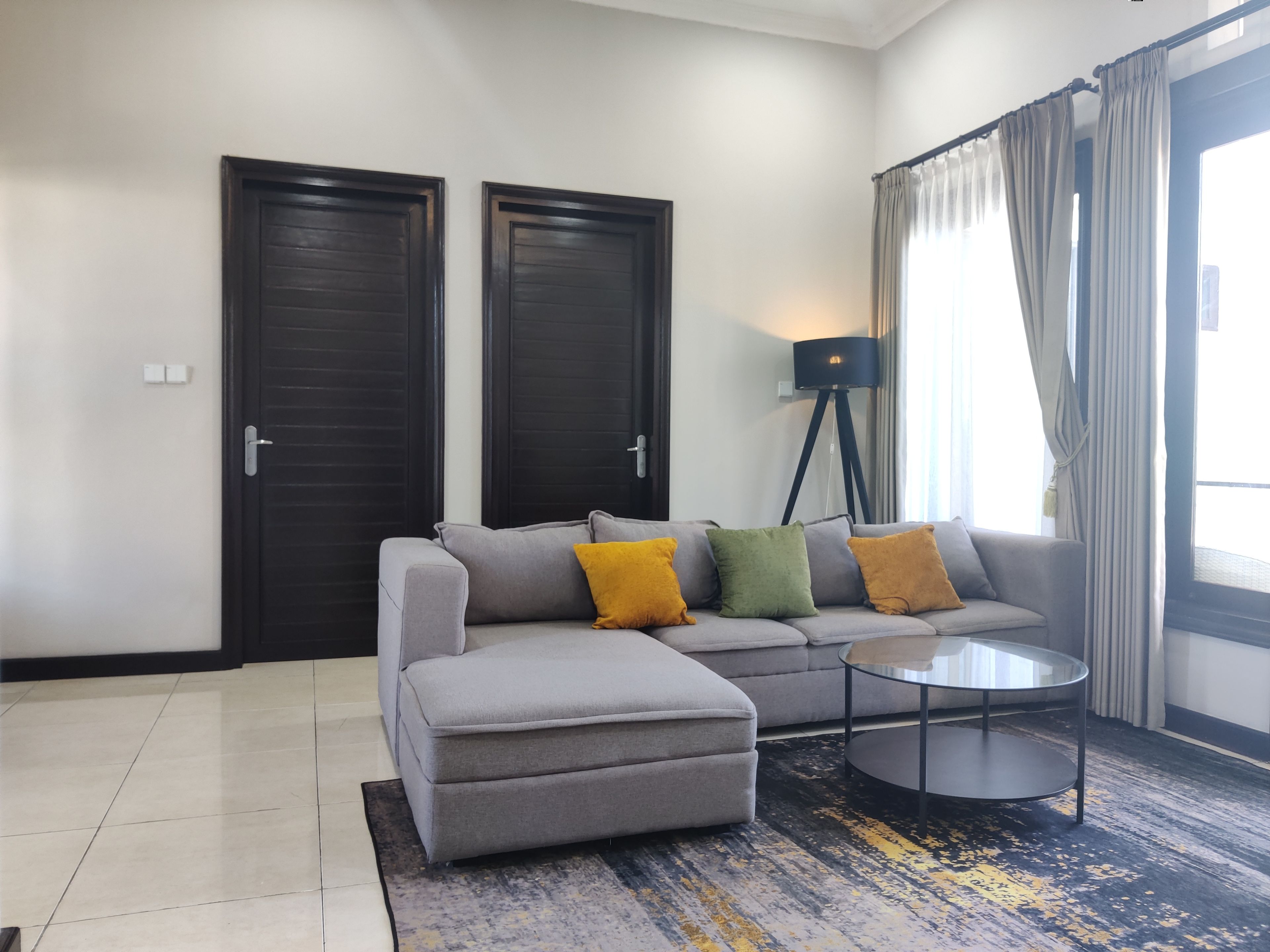 Una sala de estar moderna con un sofá gris, un pequeño reposapiés, una lámpara de pie y una mesa de centro.