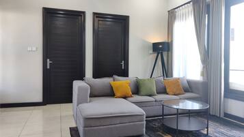 Una sala de estar moderna con un sofá gris, un pequeño reposapiés, una lámpara de pie y una mesa de centro.