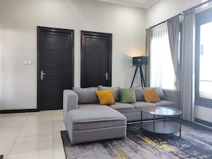 A modern living room with a grey sofa, a small ottoman, a floor lamp, and a coffee table. - Globalstay Green Villa 4BR Nusa Dua (Bali)