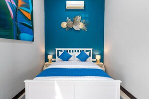 A bed with a white frame and blue bedding, flanked by two bedside lamps, against a teal wall with a decorative leaf motif. - Globalstay Green Villa 4BR Nusa Dua (Bali)