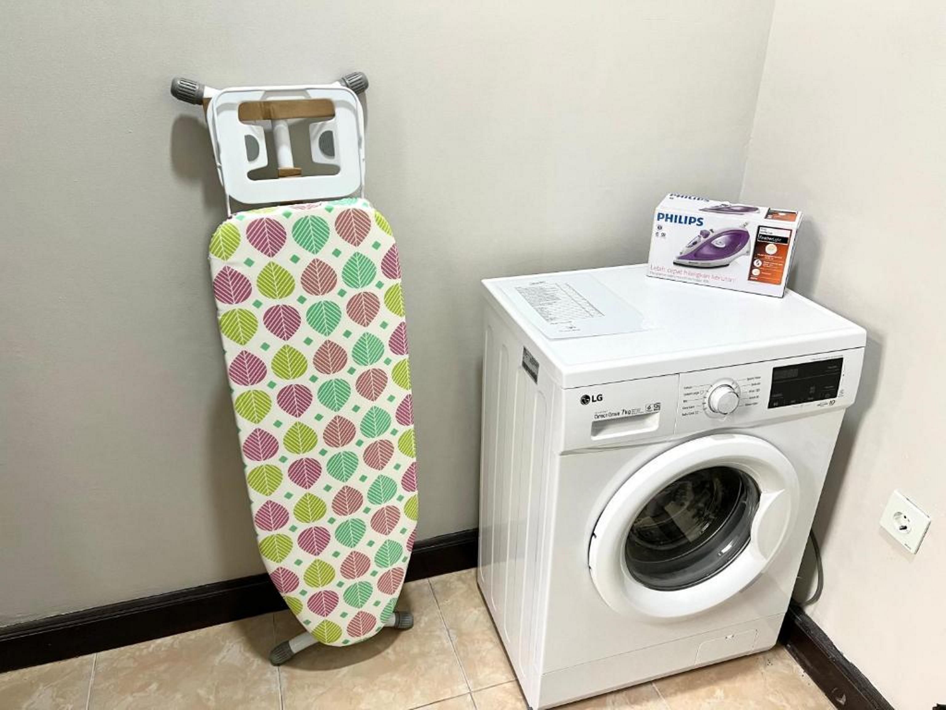 A washing machine and an ironing board in a room with a tiled floor and a plain wall.