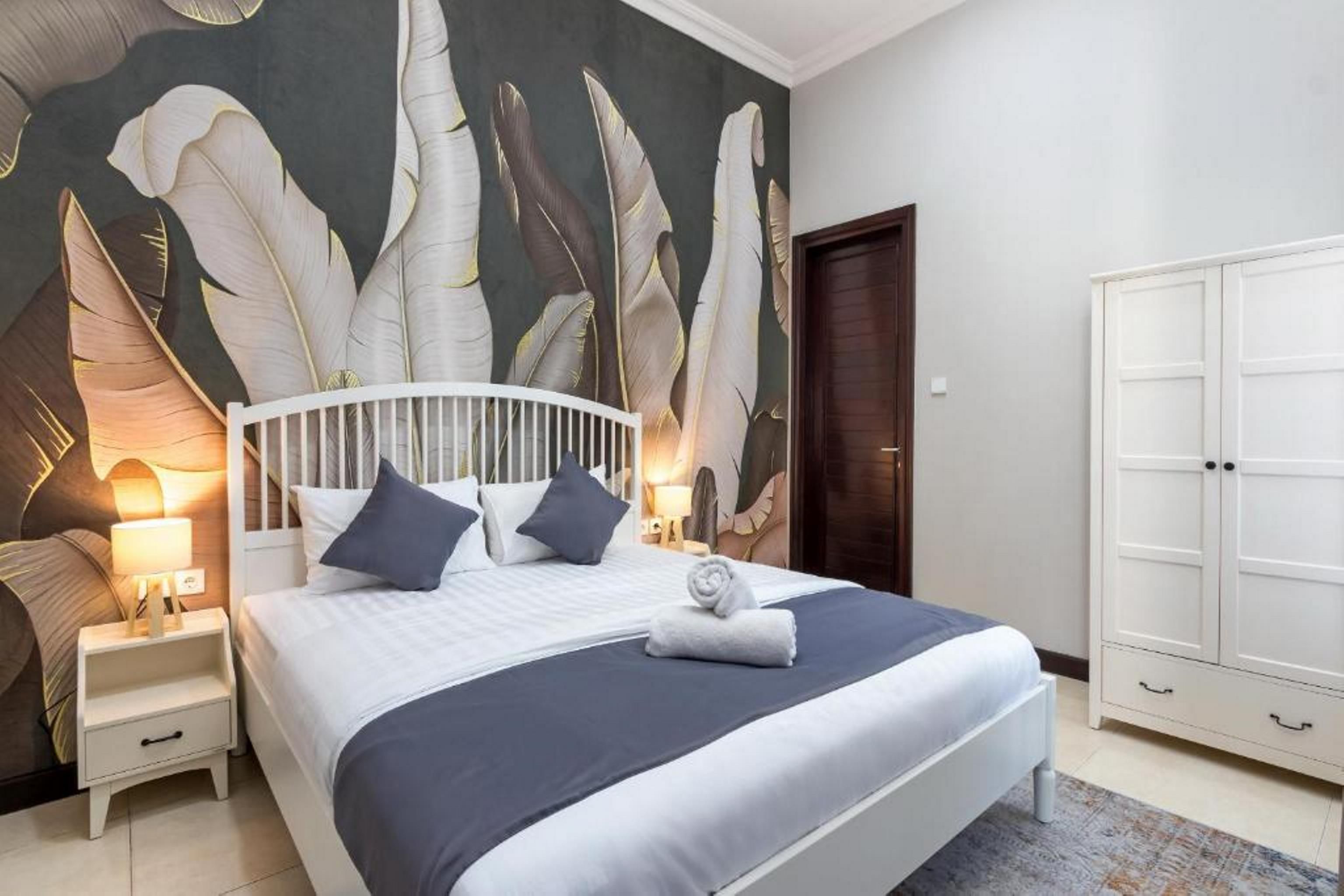 Una habitación de hotel con cama, mesitas de noche, un armario y una pared con diseño de plumas.