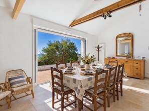 A dining area with a table set for six, wooden chairs, a vase with flowers, and a wooden cabinet with a mirror. - By the ocean, 9 guests, garden included (La Guérinière)