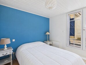 A bedroom with a bed, a nightstand, a lamp, and a window with a view of the outside. - By the ocean, 9 guests, garden included (La Guérinière)