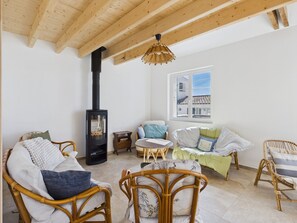 A cozy living room with wicker furniture, a black wood-burning stove, and a window with a view of buildings. - By the ocean, 9 guests, garden included (La Guérinière)