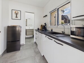 Eine moderne Küche mit weißen Schränken, einem Edelstahl-Kühlschrank, einer Spüle und einem Fenster mit Blick auf ein Haus.