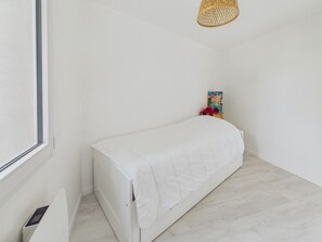 Ein schlichtes Kinderzimmer mit einem Einzelbett, einem kleinen Tisch mit Spielzeug und einem farbenfrohen Lernplakat an der Wand.