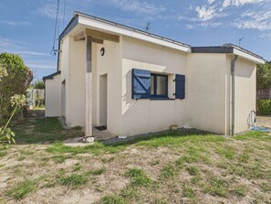 Ein eingeschossiges Haus mit Tür und Fenster mit Fensterläden, umgeben von einer Rasenfläche und einem kleinen Garten.