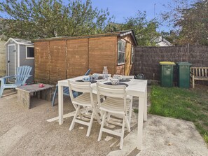 Eine Terrasse mit Tisch und Stühlen, ein Schuppen und ein Holzzaun.