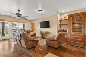 A spacious living room with a large flat-screen TV, leather recliners, a ceiling fan, and a view through the glass doors. - West Cobb- Private- sleeps 16- hot tub- petsOK (McCall)