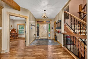 A wooden-floored hallway with a chandelier, a staircase with a metal railing, and a door with a wooden frame. - West Cobb- Private- sleeps 16- hot tub- petsOK (McCall)