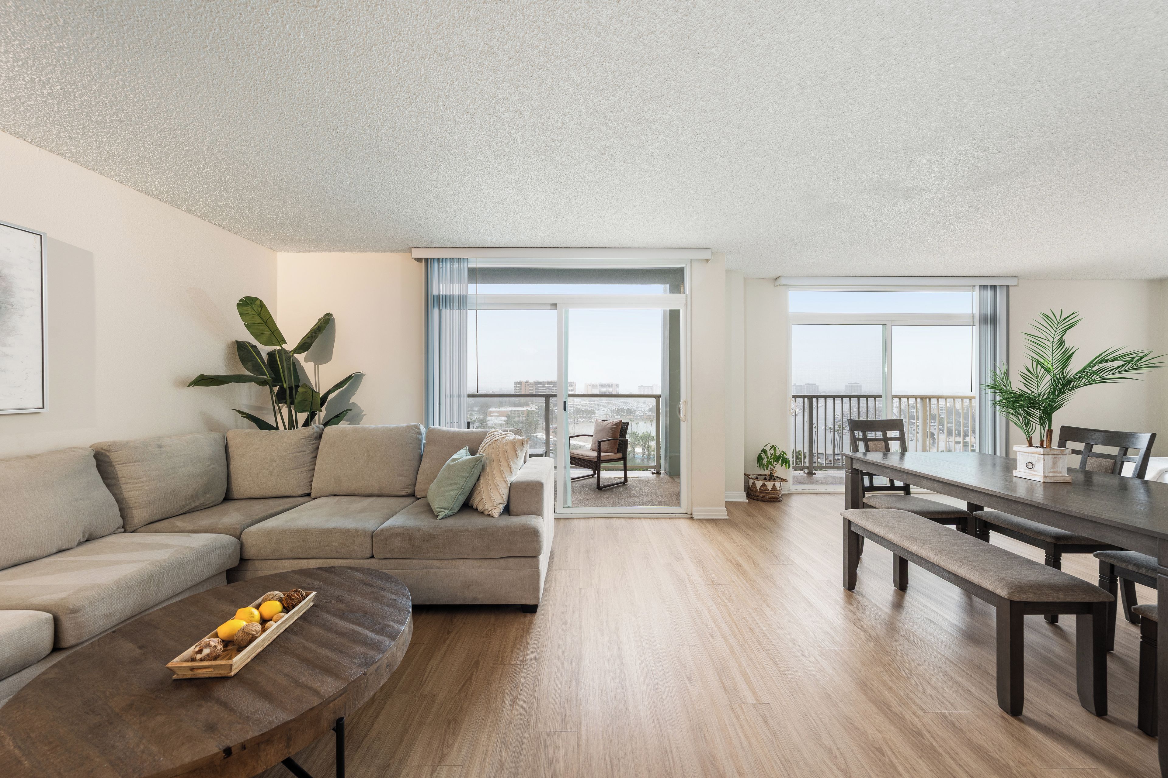 A modern living room with a sectional sofa, a dining table with benches, and a large window offering a view of the city.