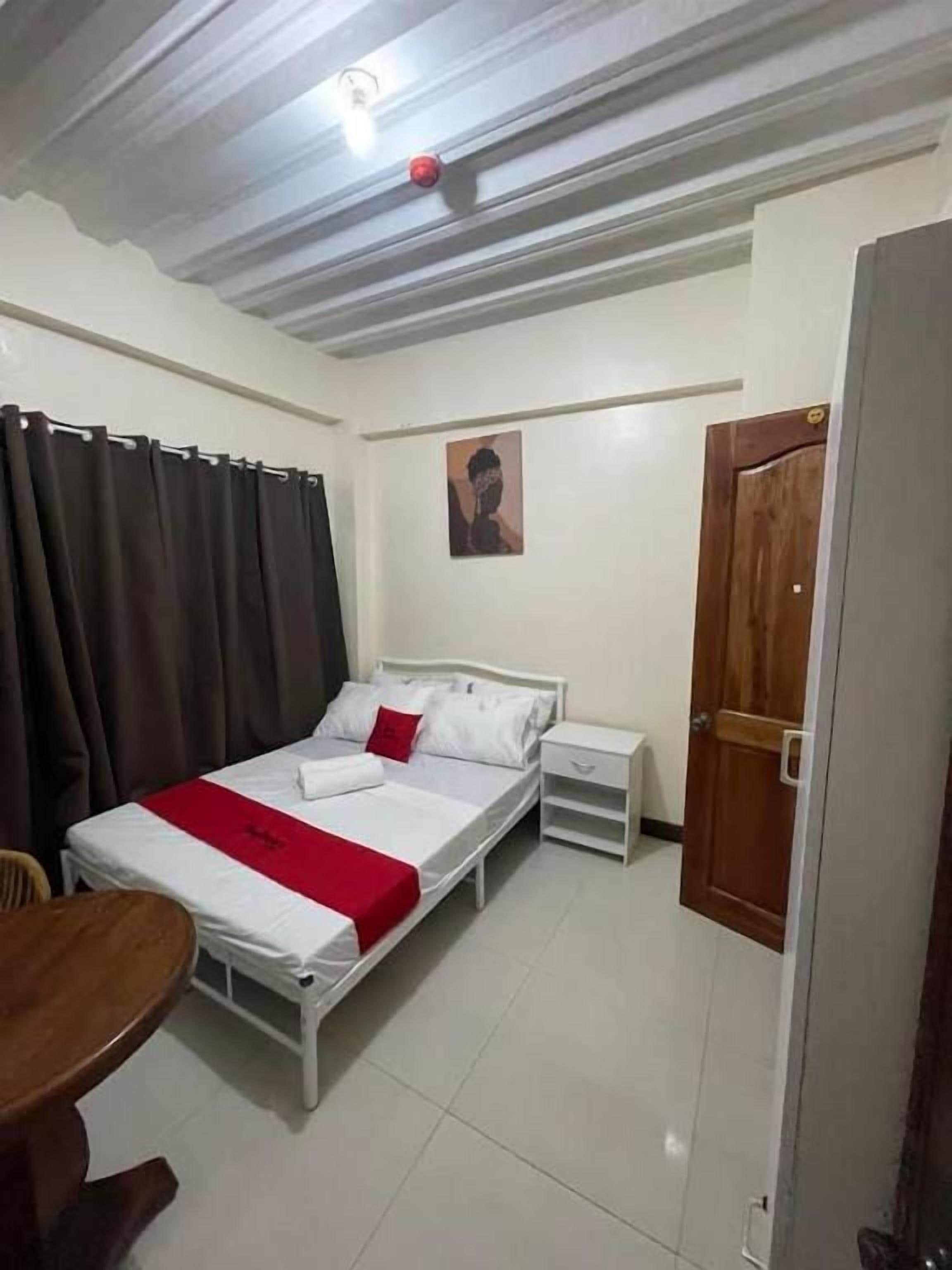 A single-bed room with a wooden headboard, a bedside table, a chair, and a red throw blanket.